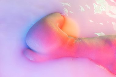 Yakın plan kadın kalçaları, süt banyosunda popolar yumuşak pembe neon ışıltılı. Güzellik, moda, tarz, vücut bakımı, kaplıca konsepti.