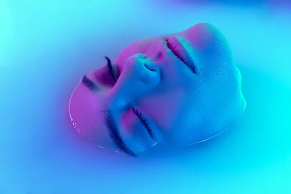 Närbild kvinnligt ansikte, ung vacker flicka i mjölkbad med mjuk glödande i blå-grön neon ljus. Skönhet, mode, stil, hudvård koncept — Stockfoto