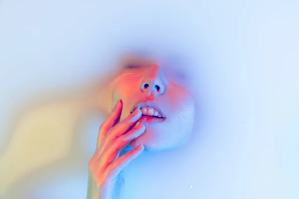 Closeup rosto feminino, jovem menina bonita no banho de leite com brilho suave em luz de néon azul-verde. Beleza, moda, estilo, conceito de cuidado da pele — Fotografia de Stock