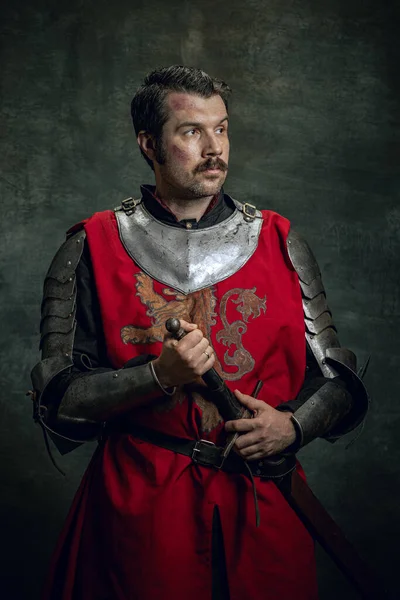 暗い背景に隔離された剣を保持汚れた負傷した顔を持つ残忍なシリアル男、中世の戦士や騎士のヴィンテージスタイルの肖像画。時代の比較 — ストック写真