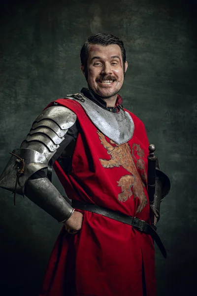 Retrato de homem sorridente em imagem de guerreiro medieval com rosto sujo ferido vestindo equipamentos isolados sobre fundo escuro. Comparação de eras — Fotografia de Stock