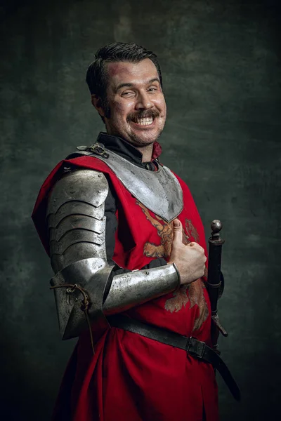 Портрет усміхненої людини на зображенні середньовічного воїна з брудно пораненим обличчям в обладнанні, ізольованому на темному тлі. Порівняння епох — стокове фото