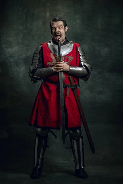 Retrato cômico de guerreiro medieval engraçado ou cavaleiro com rosto sujo ferido segurando espada isolada sobre fundo escuro. Comparação de eras — Fotografia de Stock