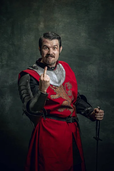 Κωμικό πορτραίτο του αστείου μεσαιωνικού πολεμιστή ή ιππότη με βρώμικο πληγωμένο πρόσωπο που εκσφενδονίζεται απομονωμένο σε σκοτεινό φόντο. Σύγκριση εποχών — Φωτογραφία Αρχείου