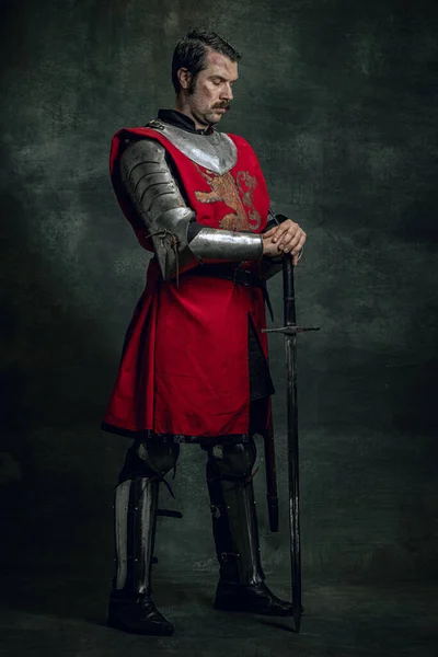 Porträt eines brutalen seriuos Mann, mittelalterlichen Krieger oder Ritter mit schmutzigem verwundetem Gesicht, das Schwert isoliert über dunklen Hintergrund hält. Epochenvergleich — Stockfoto