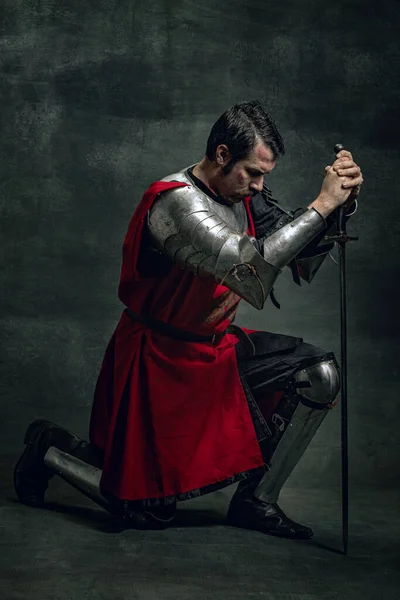 Ritratto di brutale uomo serio, guerriero medievale o cavaliere con volto sporco ferito che tiene la spada isolata su sfondo scuro. Confronto delle epoche — Foto Stock