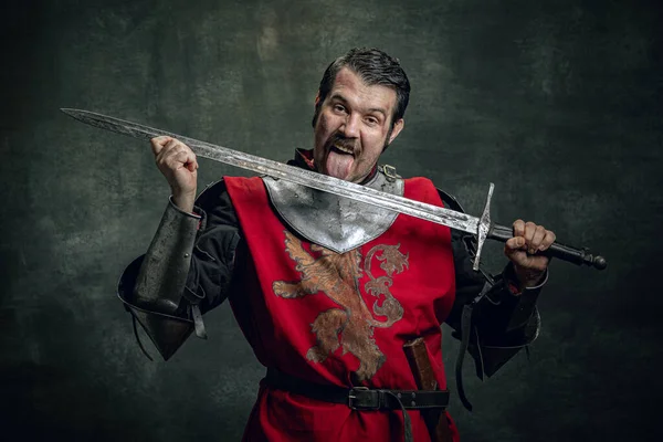 Comic porträtt av roliga medeltida krigare eller riddare med smutsiga sårade ansikte hålla svärd isolerad över mörk bakgrund. Jämförelse av tidsåldrar — Stockfoto