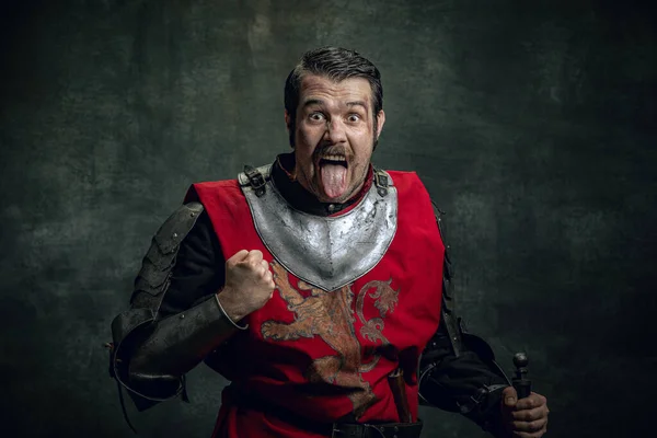 Retrato cômico de guerreiro medieval engraçado ou cavaleiro com rosto sujo ferido segurando espada isolada sobre fundo escuro. Comparação de eras — Fotografia de Stock