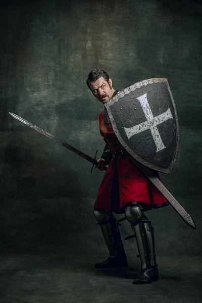 Retrato de guerrero medieval o caballero con sucia cara herida sosteniendo escudo y espada aislados sobre fondo oscuro. Comparación de épocas, historia —  Fotos de Stock