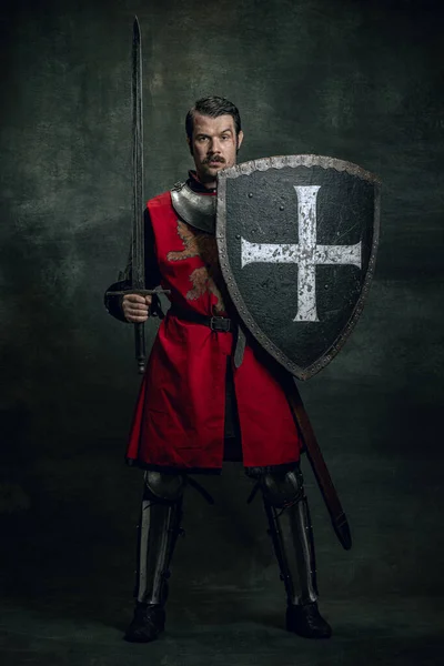Retrato de guerreiro medieval ou cavaleiro com rosto sujo ferido segurando escudo e espada isolados sobre fundo escuro. Comparação de eras, história — Fotografia de Stock