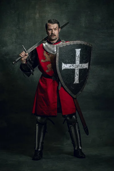 Retrato de guerreiro medieval ou cavaleiro com rosto sujo ferido segurando escudo e espada isolados sobre fundo escuro. Comparação de eras, história — Fotografia de Stock