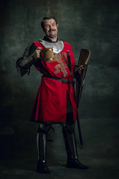 Porträt eines mittelalterlichen Kriegers oder Ritters mit schmutzigem, verwundetem Gesicht, Schild und Bierkrug isoliert vor dunklem Hintergrund haltend. Vergleich von Epochen, Geschichte — Stockfoto