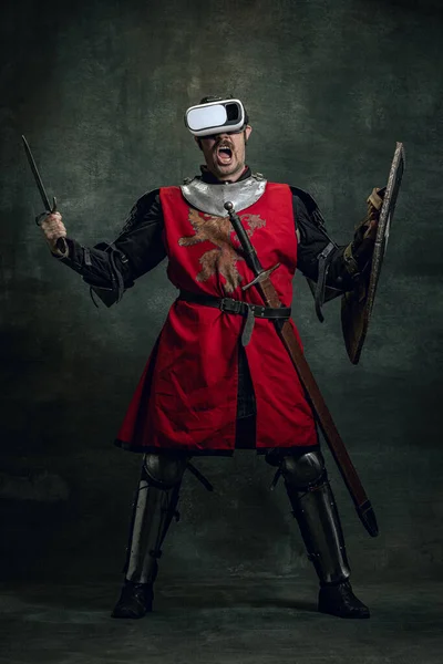 Portrét muže, středověkého válečníka, rytíře se špinavou zraněnou tváří ve VR sluchátkách izolovaných nad tmavým vinobraním. Porovnání období, historie — Stock fotografie