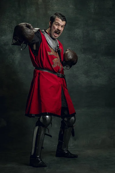 Retrato de guerreiro medieval ou cavaleiro com rosto sujo ferido em luvas de boxe isoladas sobre fundo escuro. Comparação de eras, história — Fotografia de Stock