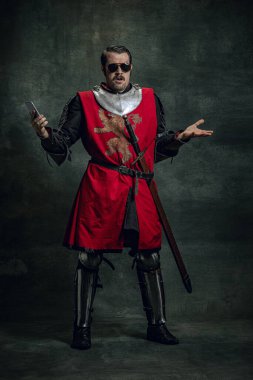 Ortaçağ savaşçısının görüntüsüne şaşırmış genç bir adam ya da karanlık arka planda izole edilmiş telefon kullanarak kirli yüzlü bir şövalye. Dönem Karşılaştırması