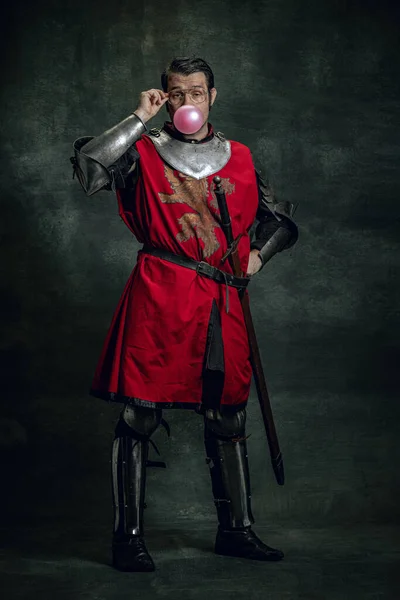 Ένας χαρούμενος μεσαιωνικός πολεμιστής ή ιππότης με βρώμικο πρόσωπο σε πολεμικό εξοπλισμό που διασκεδάζει απομονωμένος σε σκοτεινό φόντο. Σύγκριση εποχών — Φωτογραφία Αρχείου