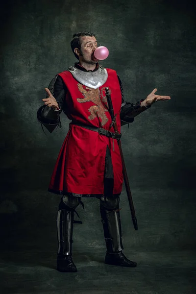 Ein fröhlicher mittelalterlicher Krieger oder Ritter mit schmutzigem Gesicht in Kriegsausrüstung, der sich isoliert vor dunklem Hintergrund amüsiert. Epochenvergleich — Stockfoto