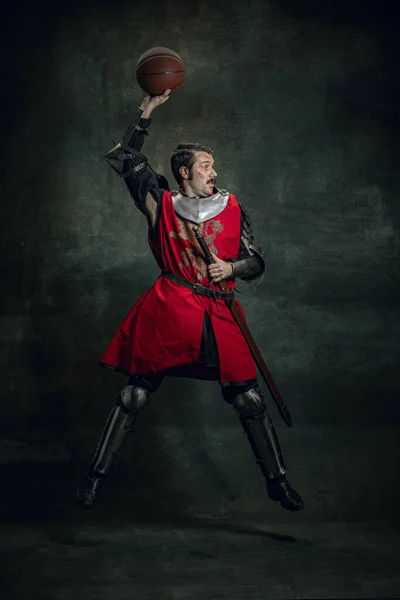 Portret średniowiecznego wojownika lub rycerza z brudną ranną twarzą bawiącego się piłką do kosza na ciemnym tle. Porównanie epok, historii — Zdjęcie stockowe