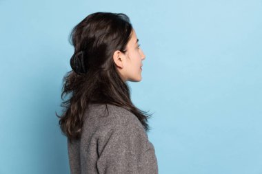 Uzun siyah saçlı, gri kazaklı, mavi arka planda izole edilmiş Hintli genç bir kız..