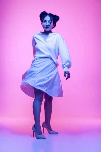 Pełnowymiarowy portret młodej pięknej dziewczyny w białym jedwabnym stroju tańczącej, latającej odizolowanej na różowym tle w neonowym świetle. Pojęcie emocji — Zdjęcie stockowe