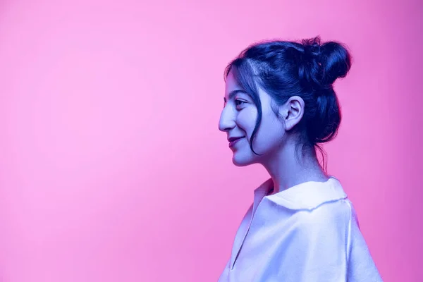 Retrato de meia-comprimento de menina bonita jovem em blusa branca posando isolado no fundo rosa em luz de néon. Conceito de emoções — Fotografia de Stock