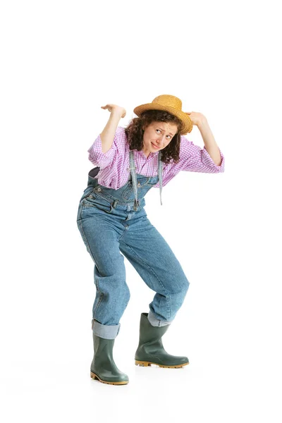 Jeune fille drôle, jardinière en uniforme de travail et chapeau montre pantomime isolé sur fond blanc. Concept d'emploi, émotions, agronomie, éco — Photo