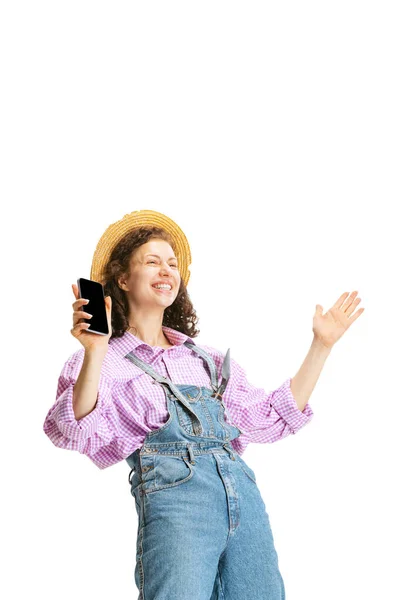 兴奋的小女孩，穿着工作服，头戴帽子的女园丁，用白色背景的电话隔离。工作概念、情感、农艺学、生态 — 图库照片