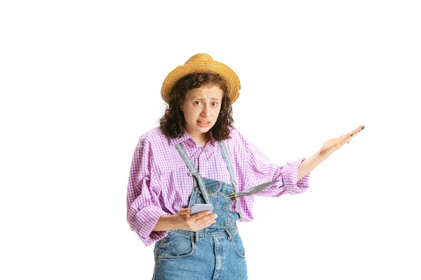 Sorpresa giovane ragazza, giardiniere donna in uniforme da lavoro e cappello utilizzando il telefono isolato su sfondo bianco. Concetto di lavoro, emozioni, agronomia, eco — Foto Stock