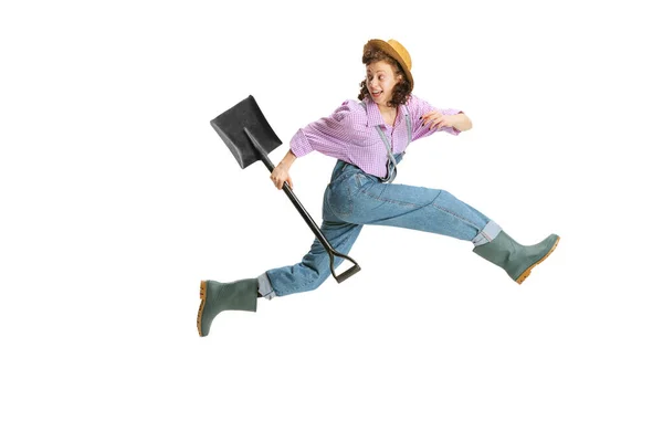 Ritratto dinamico di giovane ragazza, giardiniere donna in uniforme da lavoro e stivali di gomma che scappano isolati su sfondo bianco. Concetto di lavoro, emozioni, agronomia — Foto Stock