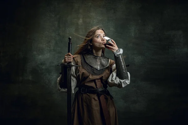 Vintage retrato de mulher adorável, guerreira medieval ou cavaleiro com sujo rosto ferido degustação de vinho isolado sobre fundo retro escuro. — Fotografia de Stock