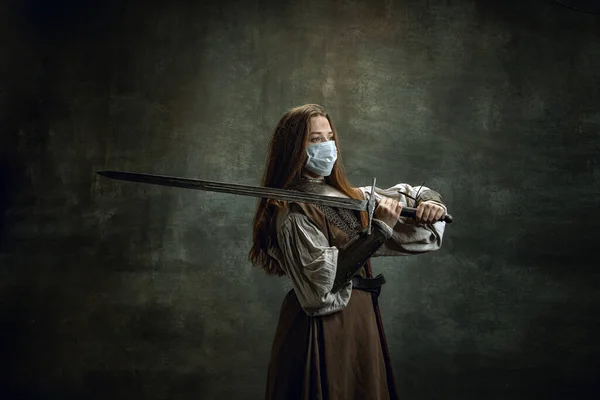 Bravo guerreiro. Vintage retrato de jovem mulher, cavaleiro medieval vestindo máscara protetora segurando grande espada isolada sobre fundo retro escuro. — Fotografia de Stock