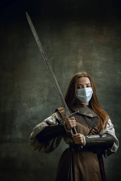 Bravo guerreiro. Vintage retrato de jovem mulher, cavaleiro medieval vestindo máscara protetora segurando grande espada isolada sobre fundo retro escuro. — Fotografia de Stock