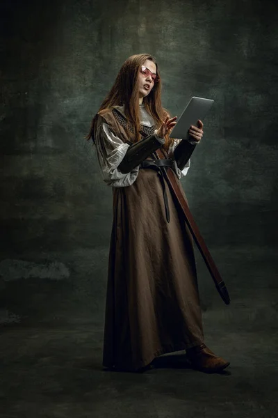 Vintage portré fiatal gyönyörű lány képére középkori háborús nő segítségével modern szerkentyű elszigetelt sötét háttérrel. A korok összehasonlítása, történelem — Stock Fotó