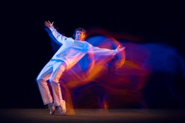 Erkek hip-hop dansçısının dinamik portresi. Karmaşık neon ışıkta koyu arka planda izole edilmiş. Gençlik kültürü, hip-hop, hareket, tarz ve moda, aksiyon.