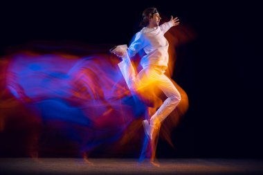 Gençlik dansı. Hip-hop dansçısının dinamik portresi, karışık neon ışıkta karanlık arka planda izole edilmiş hareket. Gençlik kültürü, hip-hop, tarz ve moda
