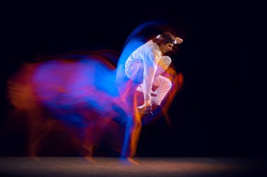 Beyaz takım elbiseli esnek bir adam karışık neon ışıkta karanlık arka planda hip-hop yapıyor. Gençlik kültürü, hip-hop, hareket, tarz ve moda, aksiyon.