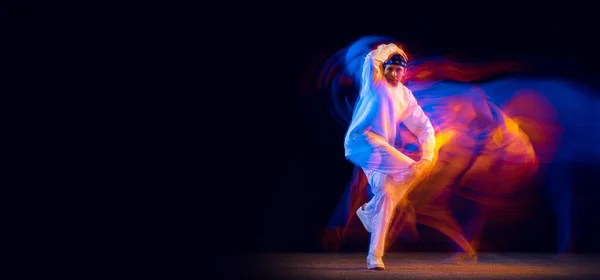 身穿白色运动服的时髦男子在混合霓虹灯下与深色背景隔离，跳嘻哈舞。青年文化、嘻哈、运动、风格和时尚、行动. — 图库照片