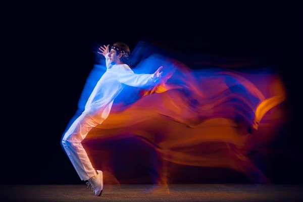 Stylový muž v bílém sportovním obleku tančící hip-hop izolovaný na tmavém pozadí ve smíšeném neonovém světle. Mládež kultura, hip-hop, pohyb, styl a móda, akce. — Stock fotografie