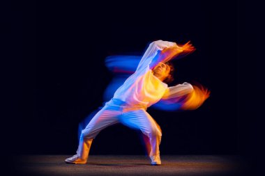Gençlik dansı. Hip-hop dansçısının dinamik portresi, karışık neon ışıkta karanlık arka planda izole edilmiş hareket. Gençlik kültürü, hip-hop, tarz ve moda