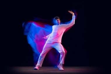 Gençlik dansı. Hip-hop dansçısının dinamik portresi, karışık neon ışıkta karanlık arka planda izole edilmiş hareket. Gençlik kültürü, hip-hop, tarz ve moda