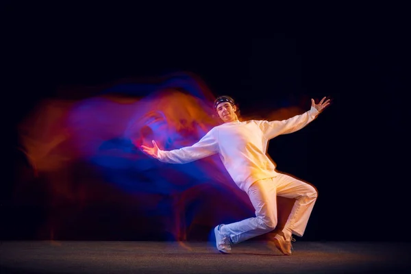 Retrato dinâmico de dançarino de hip-hop masculino dançando isolado em fundo escuro em luz de néon mista. Cultura juvenil, hip-hop, movimento, estilo e moda, ação. — Fotografia de Stock