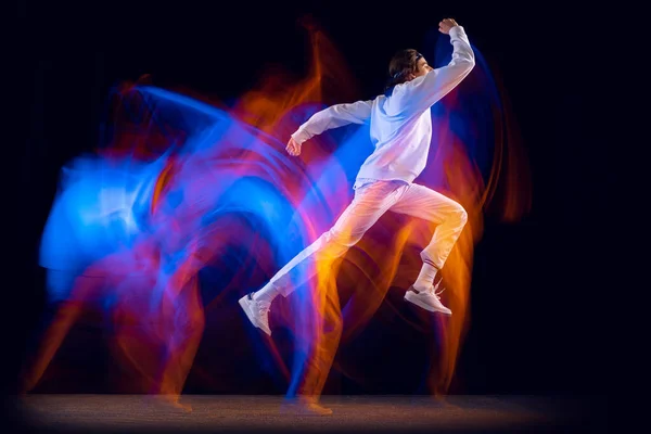 Гибкий человек в спортивном белом костюме танцующий хип-хоп изолирован на тёмном фоне в смешанном неоновом свете. Молодежная культура, хип-хоп, движение, стиль и мода, экшн. — стоковое фото