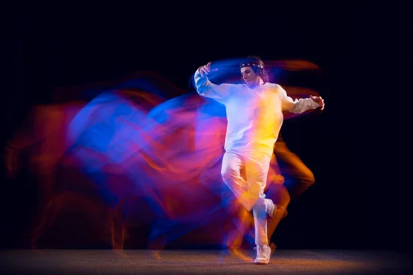 Dynamický portrét mužské hip-hopové tanečnice tančící izolovaně na tmavém pozadí ve smíšeném neonovém světle. Mládež kultura, hip-hop, pohyb, styl a móda, akce. — Stock fotografie
