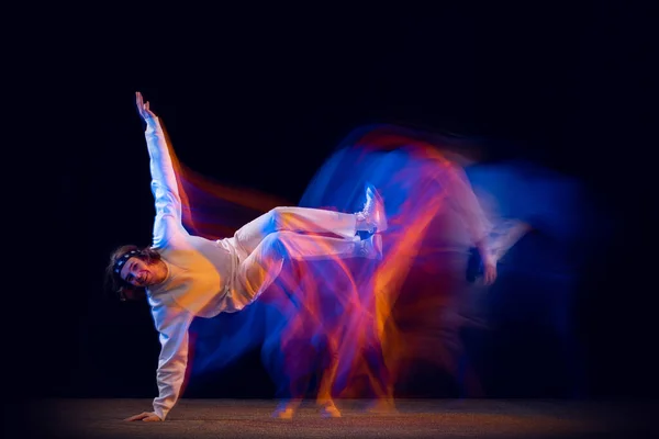 Stijlvolle man in sportwit pak dansend hiphop geïsoleerd op donkere achtergrond in gemengd neonlicht. Jeugdcultuur, hiphop, beweging, stijl en mode, actie. — Stockfoto
