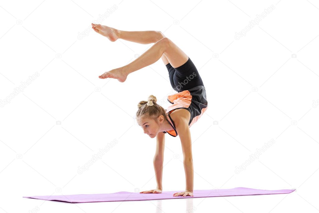 One flexible young girl, rhythmic gymnastics artist practicing isolated on white studio background. Grace in motion, action. Doing exercises in flexibility.