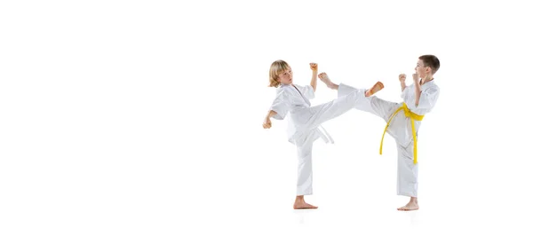 İki küçük çocuğun dinamik portresi, tekvando ya da beyaz arka planda izole edilmiş doboks eğitimi alan karate sporcuları. Spor anlayışı, dövüş sanatları — Stok fotoğraf