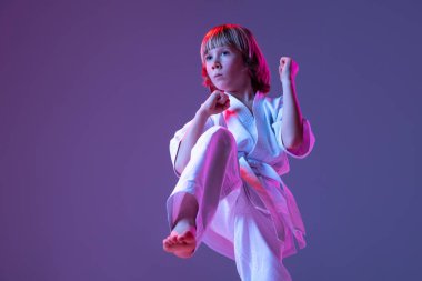 Çocuğun dinamik portresi, genç erkek tekvando, Doboks takımındaki karate atletleri neon rengi mor arka planda izole edilmiş temel hareketleri yapıyorlar. Spor anlayışı, dövüş sanatları