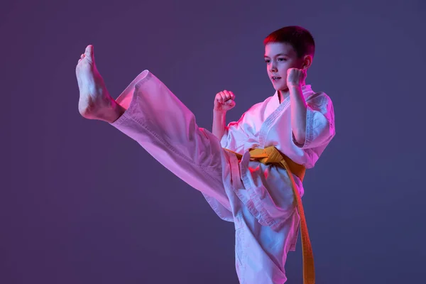 Portret van sportieve jongen, mannelijke taekwondo, karate atleten in doboks doen basisbewegingen geïsoleerd op paarse achtergrond in neon. Begrip sport, vechtsport — Stockfoto