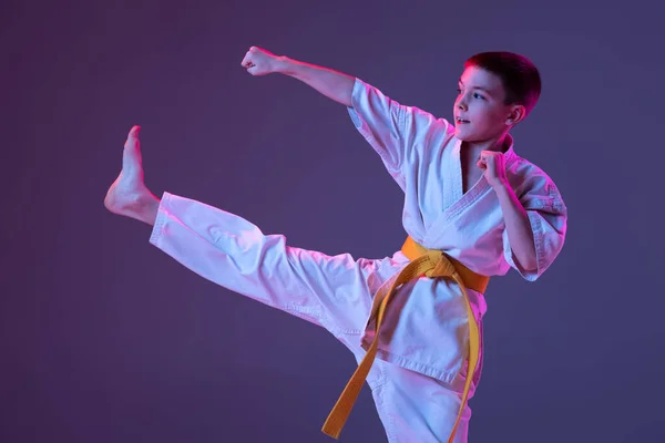 Portret van sportieve jongen, mannelijke taekwondo, karate atleten in doboks doen basisbewegingen geïsoleerd op paarse achtergrond in neon. Begrip sport, vechtsport — Stockfoto