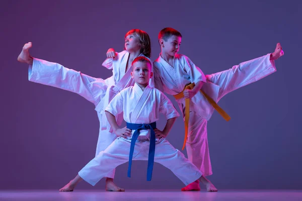 Três crianças esportivas, meninos, taekwondo ou atletas de karatê em doboks posando isolados em fundo de cor muito peri em néon. Conceito de esporte, artes marciais — Fotografia de Stock
